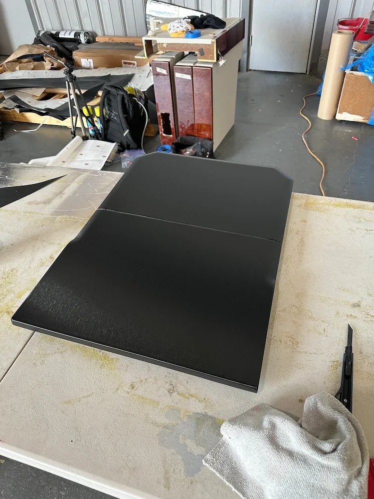 A closed black laptop on a dusty white work table in a workshop or garage setting.