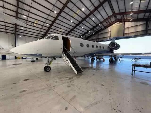 A private jet inside an aircraft hangar with a staircase leading to the entrance door.