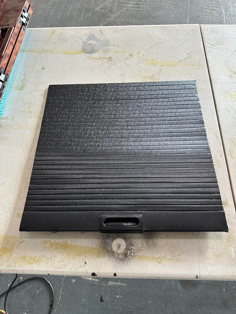 A black, rectangular ramp with ridges, placed on a workbench in a workshop.