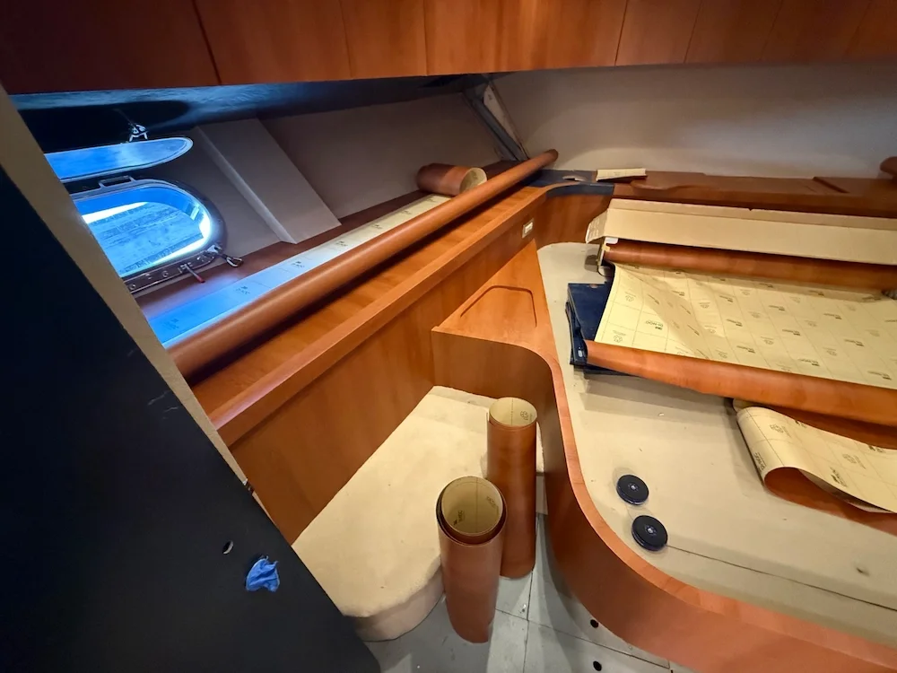 Interior of a boat or yacht under renovation, showing wooden panels, rolled-up sheets of blueprints or wallpaper, and various tools and materials.
