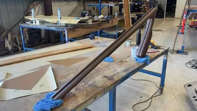 Wooden tube and parts on workbench in woodworking shop, with tools and materials around.