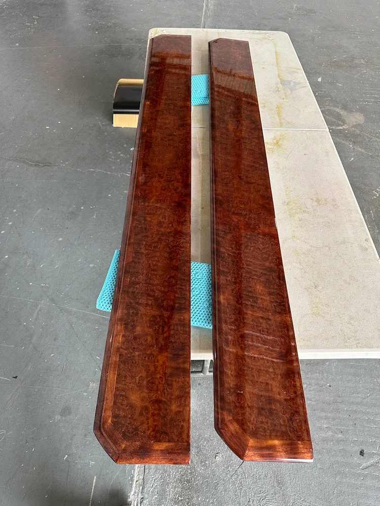 Two polished wooden pieces placed parallel on a table with a concrete floor in the background.