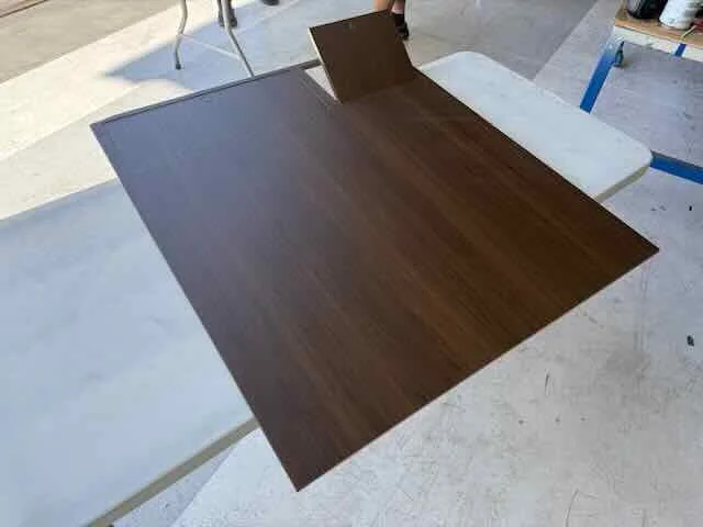 A wooden table with a darker brown surface and a light-colored cloth-covered surface near it, set on a concrete or stone floor.