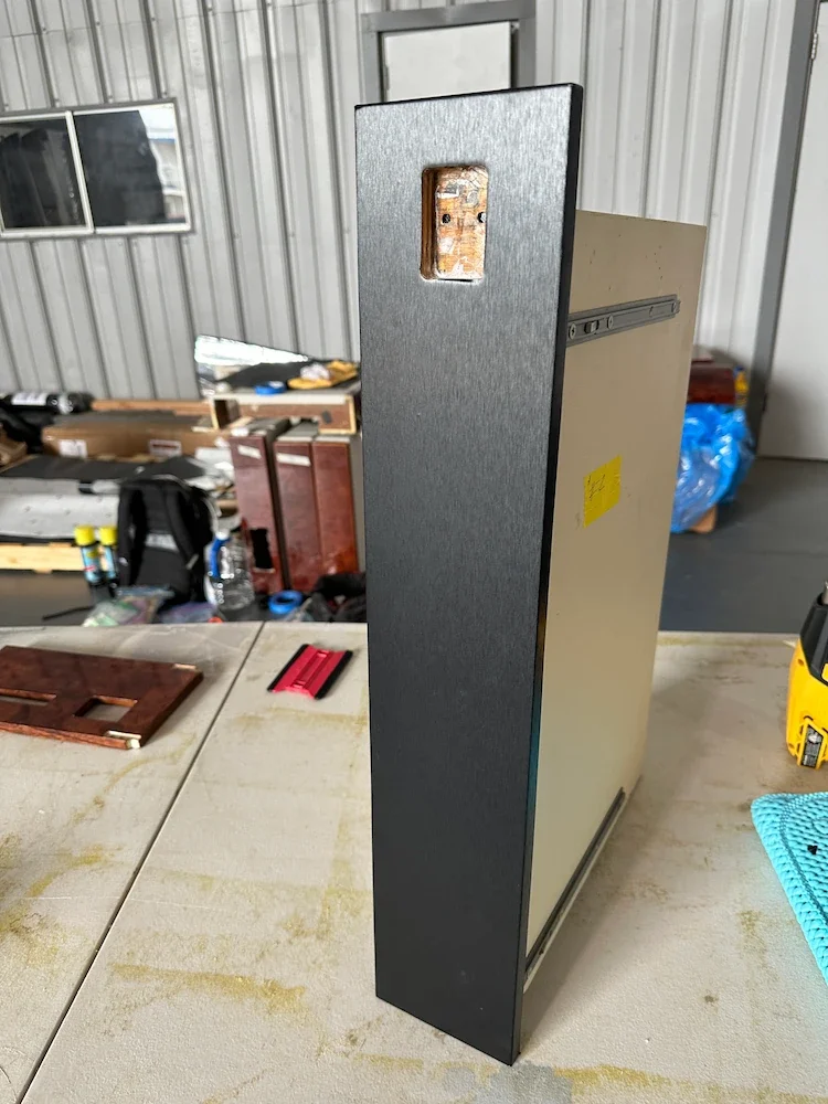 Tall metal cabinet with an open electrical outlet on the back in a workshop or storage space.