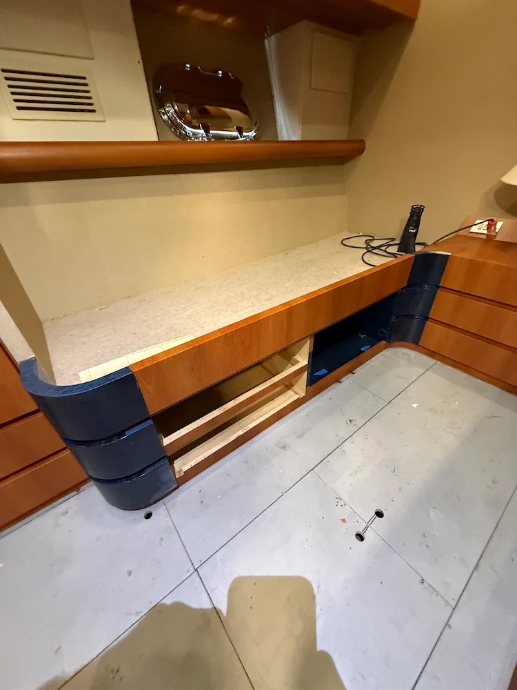 Room with a wooden countertop, a black and wooden corner desk, a wall-mounted mirror, and various electronic devices on the surface.