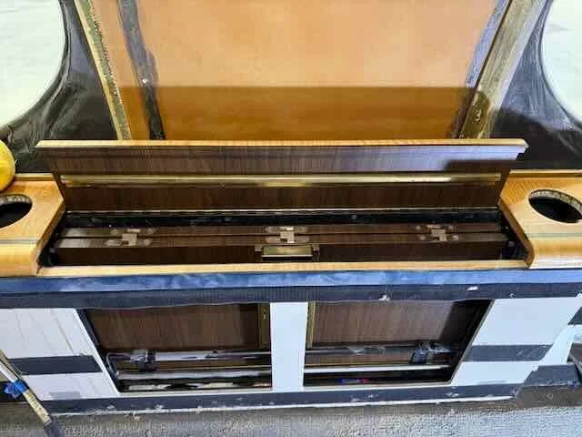 An empty vintage upright piano with a wooden top and open lid, showing internal strings and hammers, situated between two shelves with cup holders.