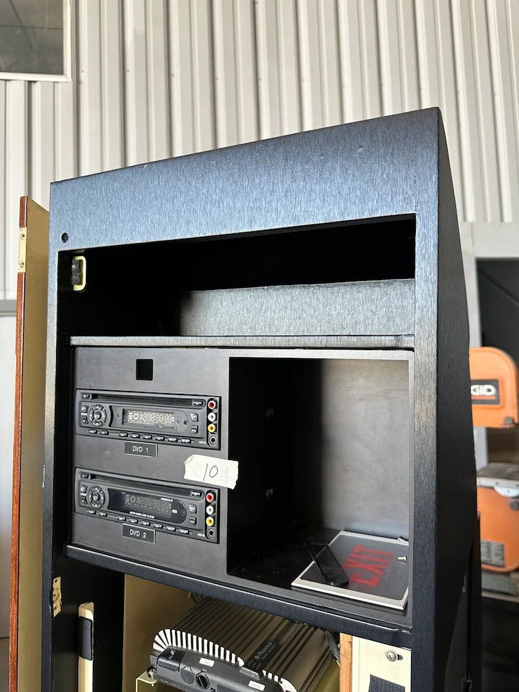 View of a black cabinet with two DVD players labeled 'DVD 1' and 'DVD 2', a small white label with the number '10', and a remote control with a red 'Caution' sign at the bottom.