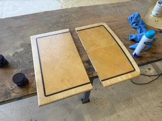 Two wooden tabletop sections with black border in progress of assembly on a workbench, with tools and materials nearby.
