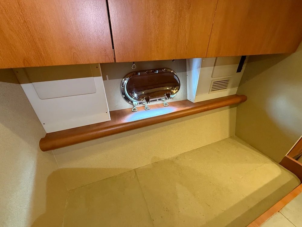 View of a room with a wooden cabinet above a beige floor, containing a small metallic hatch, a white panel, and some vents.