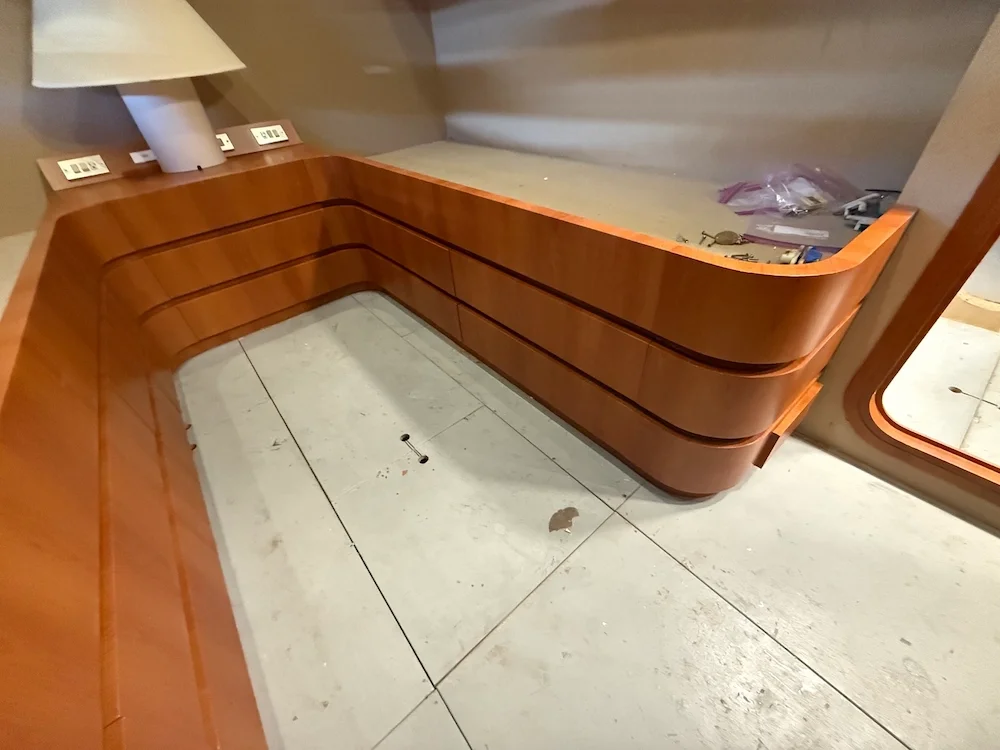 Wooden reception desk with built-in outlets and a lamp on a side table in a room under construction.