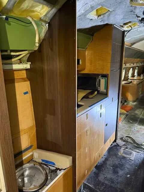 Interior of a vintage camper or RV with wooden cabinetry, a small microwave, and a stainless steel sink.