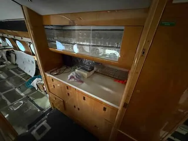 Interior of an aircraft with a wooden cabinet and a window, showing parts of the aircraft interior and a seat to the left.
