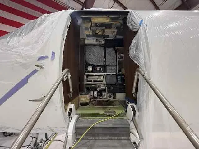 The interior of an aircraft cockpit and cabin with plastic coverings, taken from the plane's entrance.