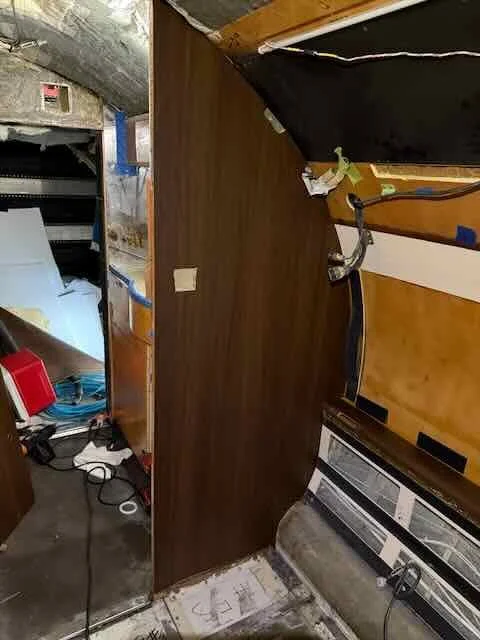 Interior of a room under renovation, showing a cluttered workspace with tools, electrical cords, and partially finished drywall.