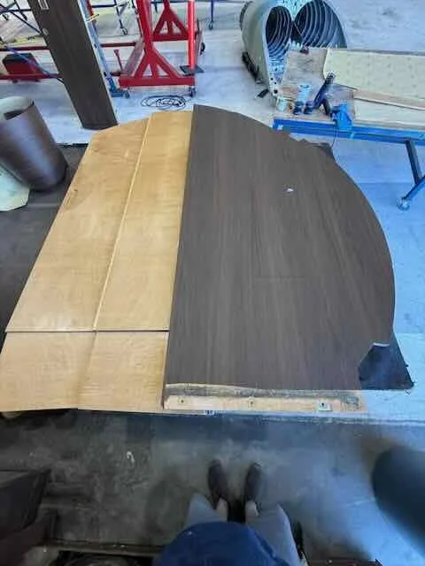 Two large wooden tables in a workshop, one with a light wood finish and the other with a dark wood finish, partially assembled.