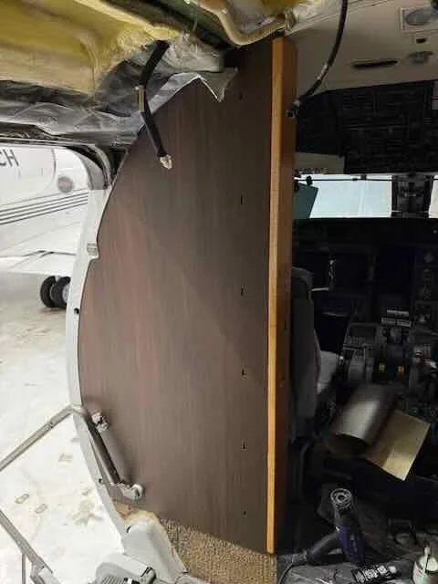 Interior view of an aircraft cockpit with a wooden panel or partition installed inside.