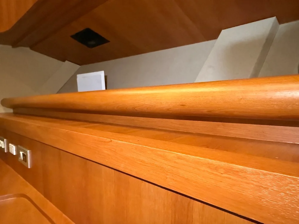 Close-up view of a polished wooden shelf or counter inside a room, with a wall and part of the ceiling in the background.