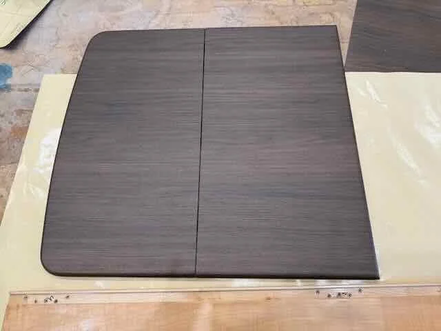 A dark wooden dining table with rounded edges, set on a light-colored floor with some additional wooden pieces underneath.