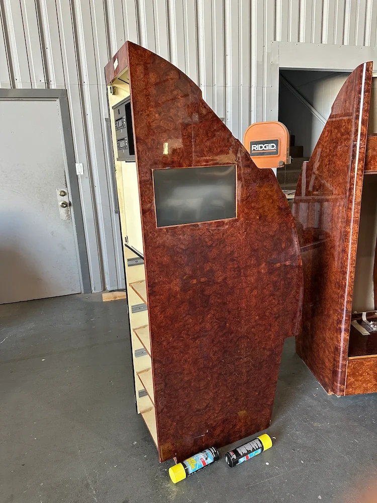 A wooden privacy booth with a small screen on the front, located in a warehouse or storage area.