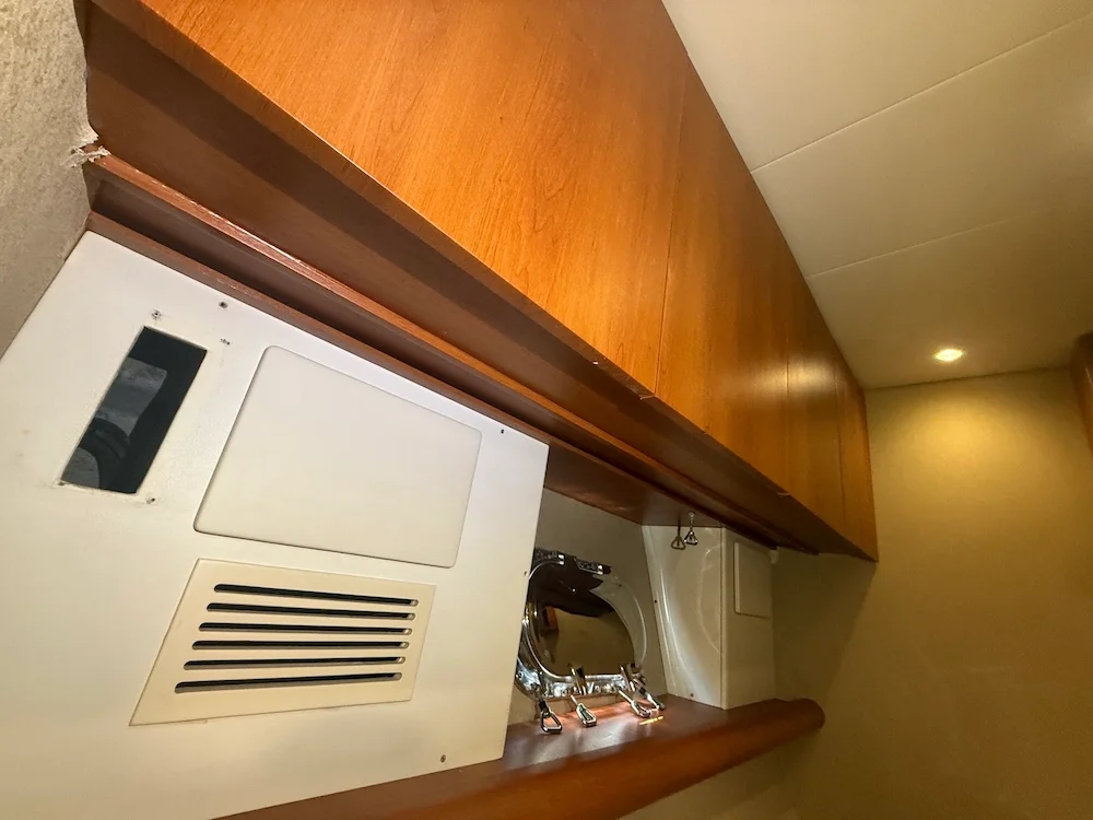 A laundry room with a washing machine, a wooden cabinet above, and a vent on the front panel of the machine.