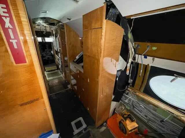 Inside a damaged vehicle, with broken wooden cabinets, a burned ceiling, and scattered equipment, indicating a fire damage interior.