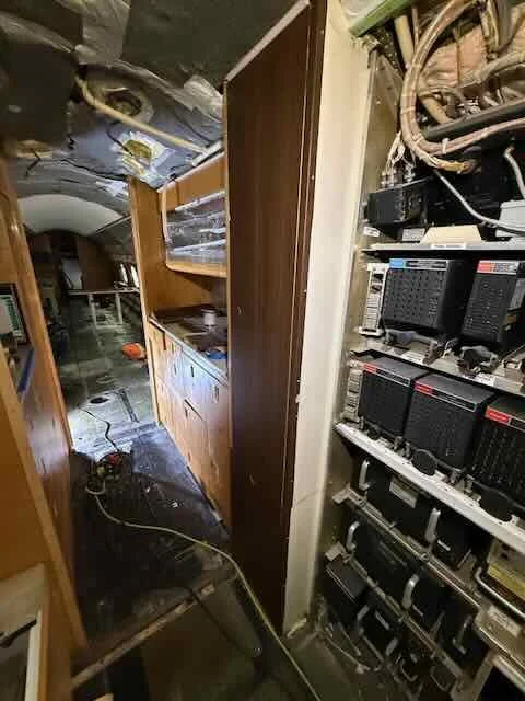 Interior of a damaged RV or van with electrical panels, wires, and a cluttered interior visible.