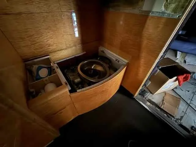 A small laundry area with a front-loading washing machine, wooden cabinetry, and some storage boxes on the side.