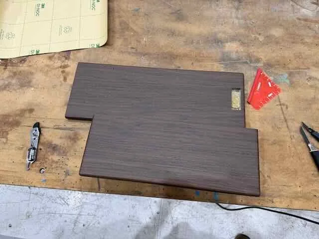 Two dark wooden pieces on a workbench with tools and a notebook nearby.