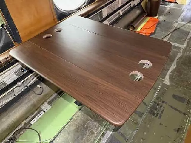 Wooden tabletop with three holes cut out, placed on a manufacturing or assembly line in a workshop.