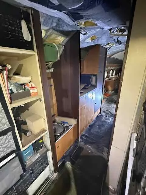 Interior view of a room with shelves, cabinets, and a countertop, all covered in soot and debris, indicating fire damage.