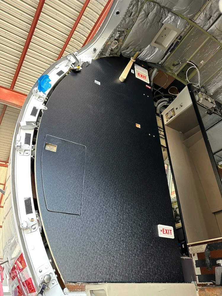 Interior view of an aircraft cockpit showing the ceiling, with some insulation and emergency exit signs on the floor.