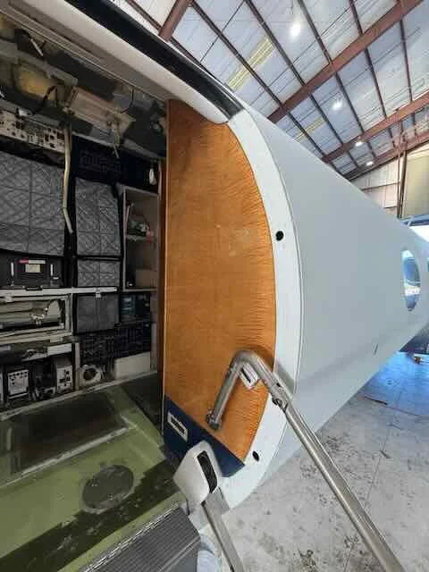 Inside a spacecraft or satellite module, with electronic equipment, cabinets, and a curved metallic exterior wall.