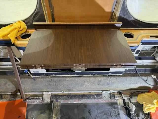 View of a partially assembled piece of furniture, possibly a table, with a dark wood finish, in a workshop or repair shop, surrounded by tools and equipment.