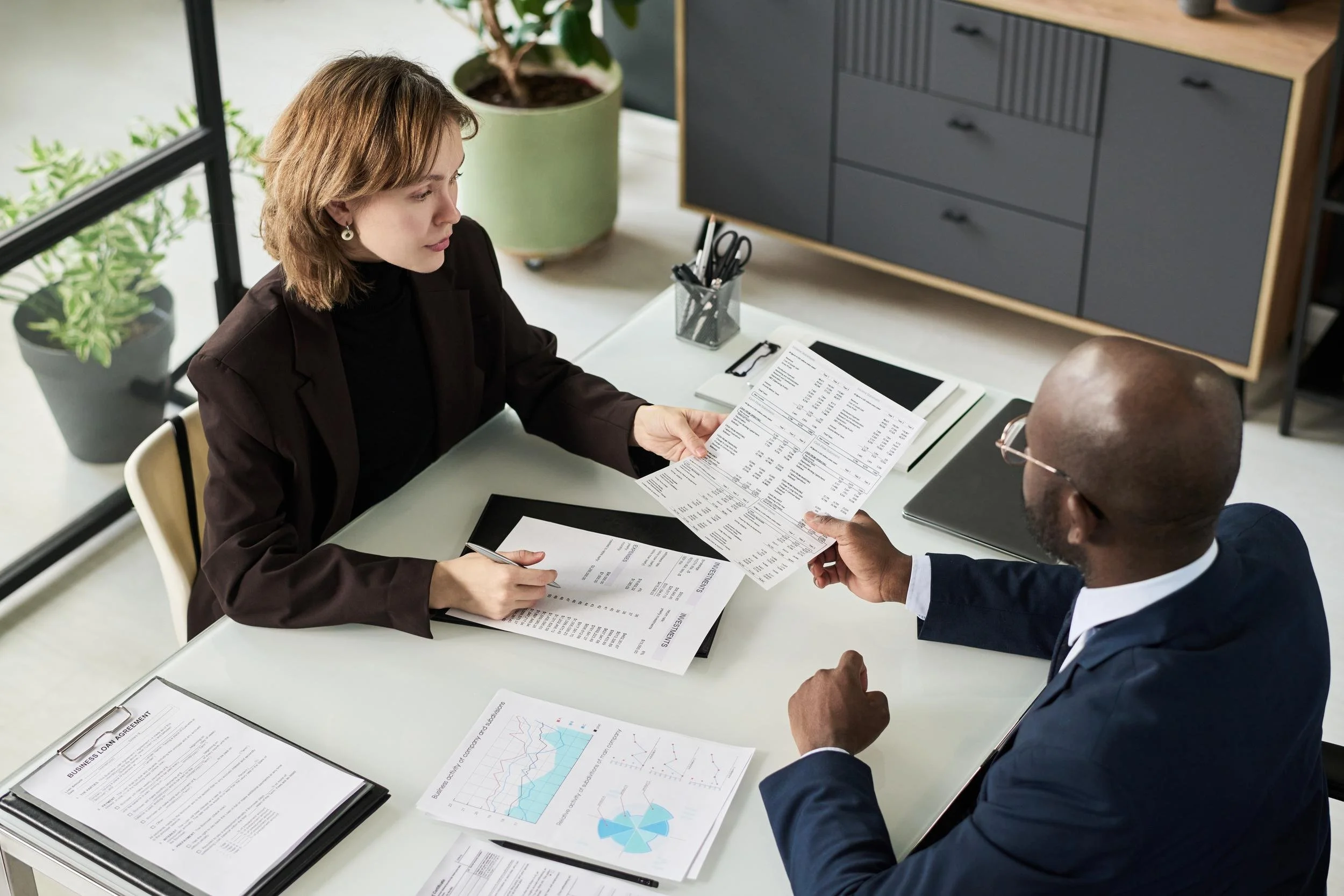 Two people exchanging documents at a business meeting in a modern office.