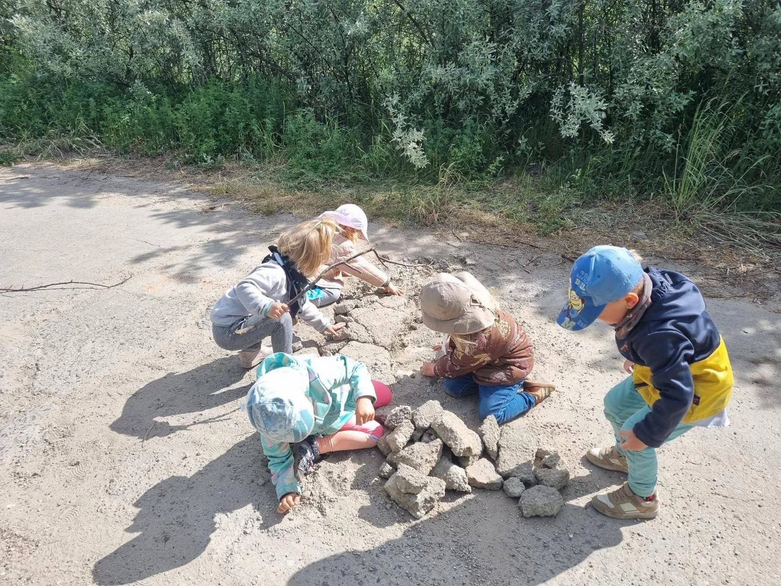 Fünf Kinder spielen das Sand und Steine auf einem Weg in der Natur.