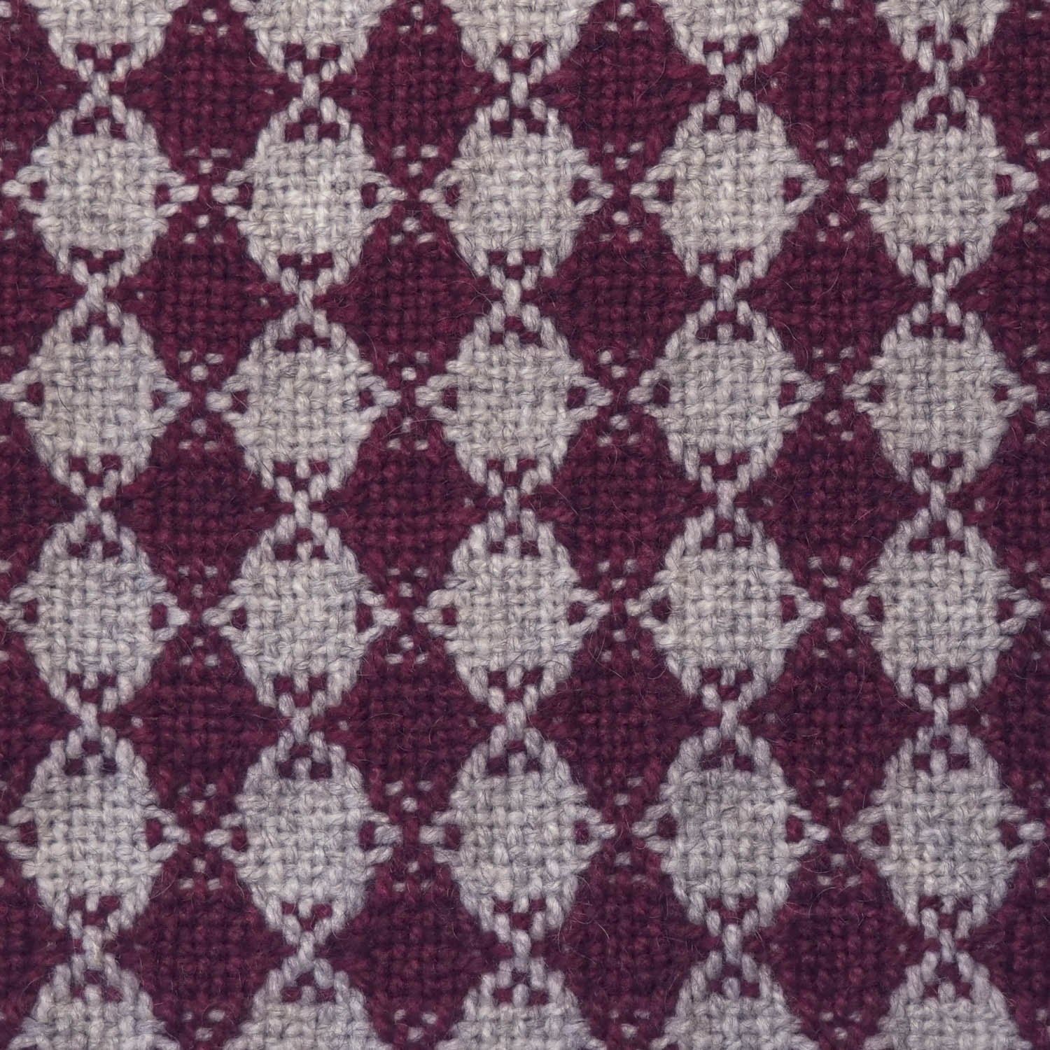 Close-up of handwoven fabric with a repeating geometric pattern of plum diamonds and beige diamonds with circular edges.