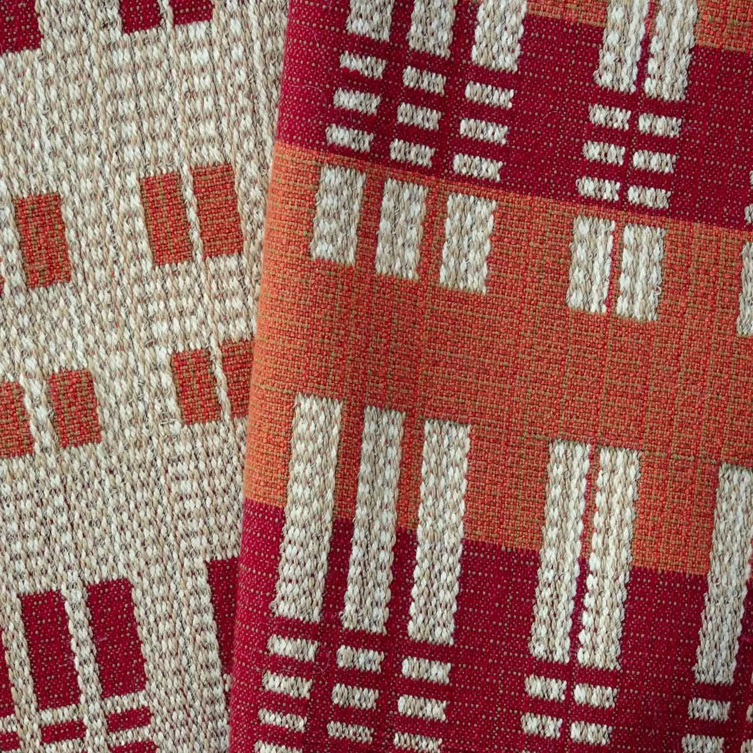Close-up of both sides of a handwoven fabric with a geometric pattern in red, beige, and orange tones. Crafted by Karen Donde of Asheville, NC.