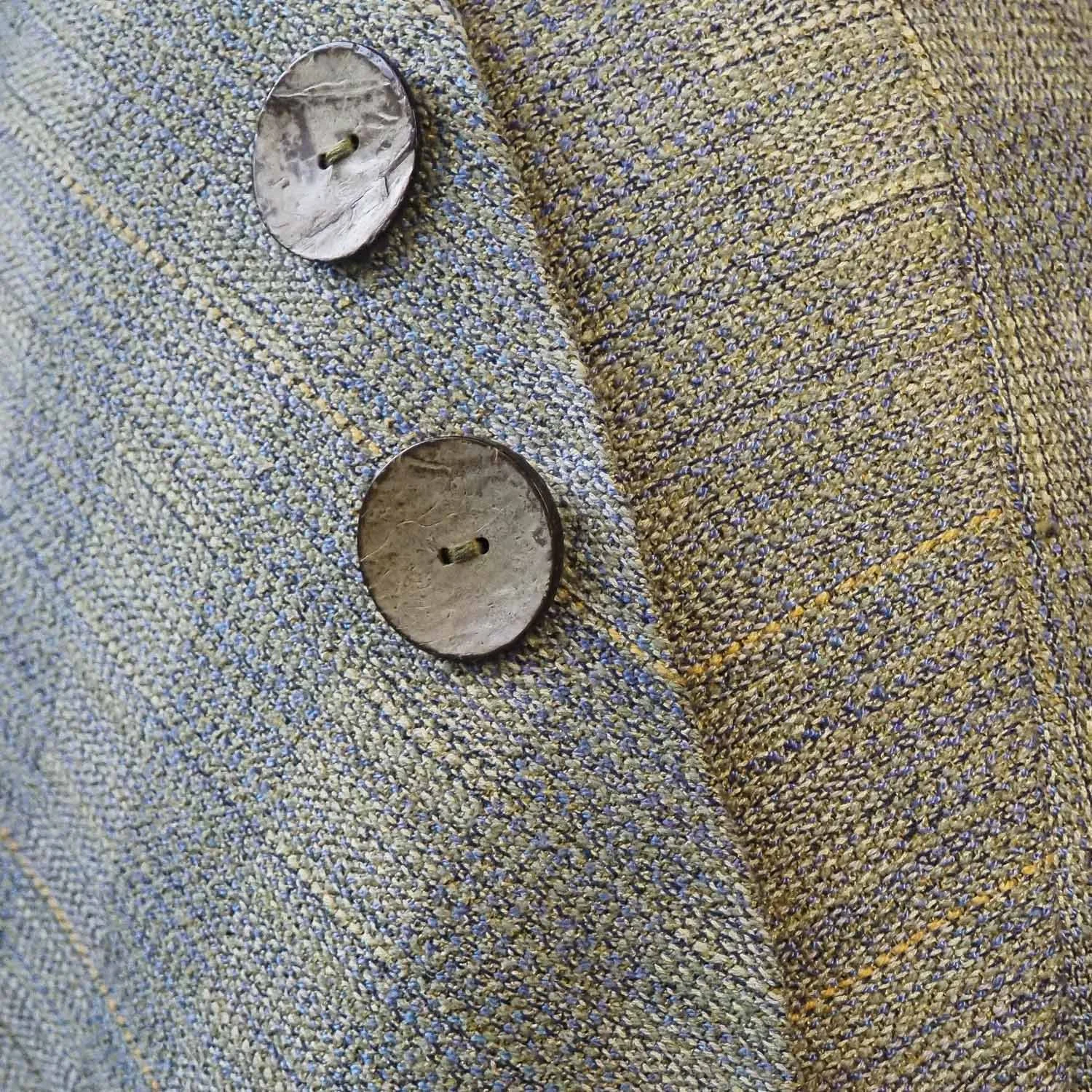 Close-up of two round wooden buttons sewn onto a handwoven finely textured, multicolored fabric, with a pattern of small, tightly woven fibers.