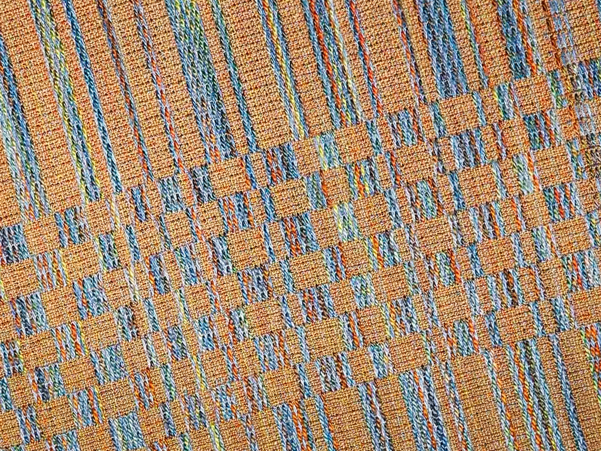 Close-up of a textured handwoven woven fabric with a plaid pattern in shades of orange, blue, green, and yellow.