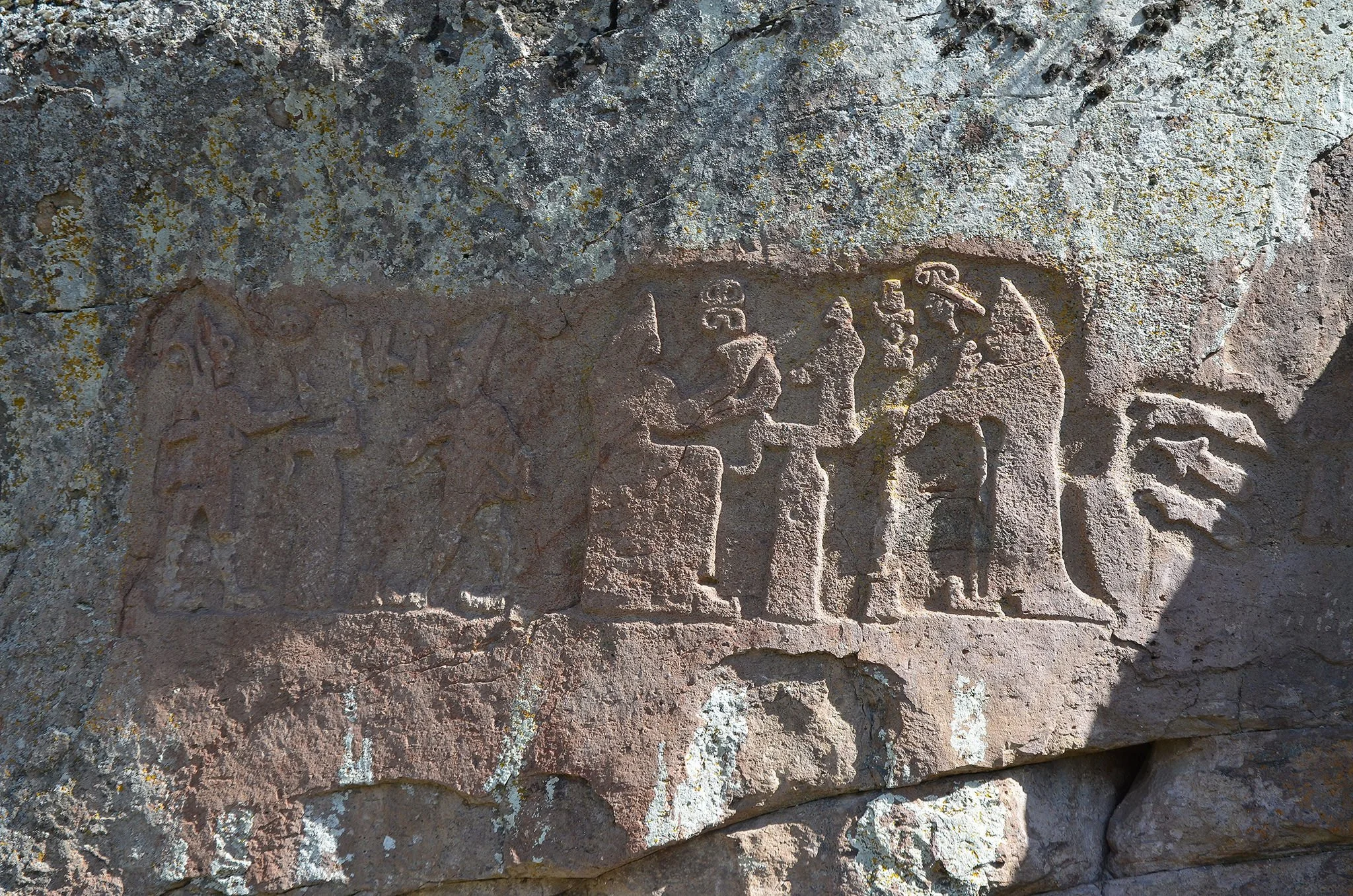 Close-up of ancient carved stone engravings on a weathered rock surface, with lichen and moss growing around the carvings.