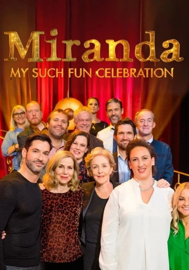 Group photo of people standing together on stage at Miranda: My Such Fun Celebration, with red curtains and a gold and red sign in the background.