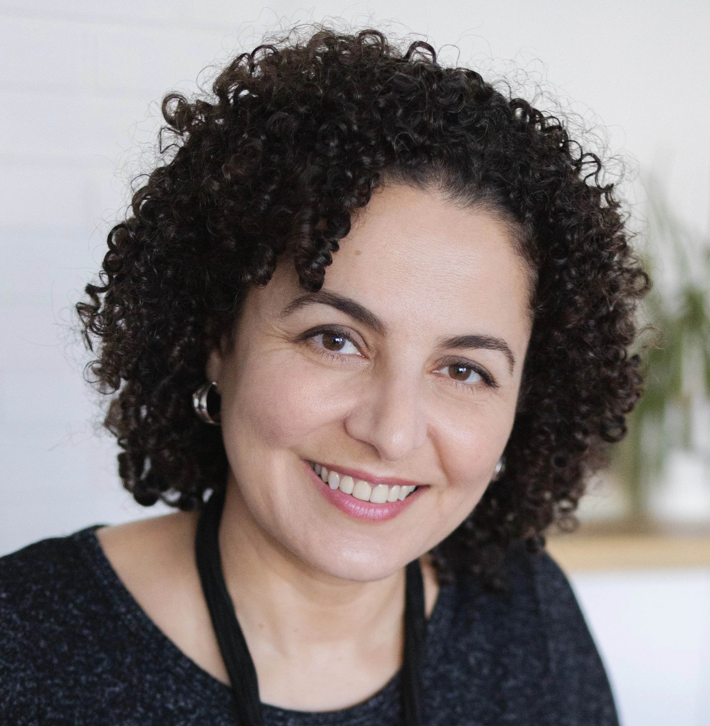 Close-up of a woman's face with curly dark hair, smiling, wearing a black top.
