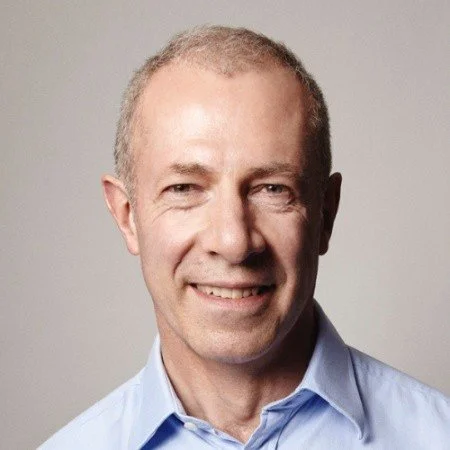A portrait of a middle-aged man with short, light-colored hair wearing a blue dress shirt, smiling at the camera.