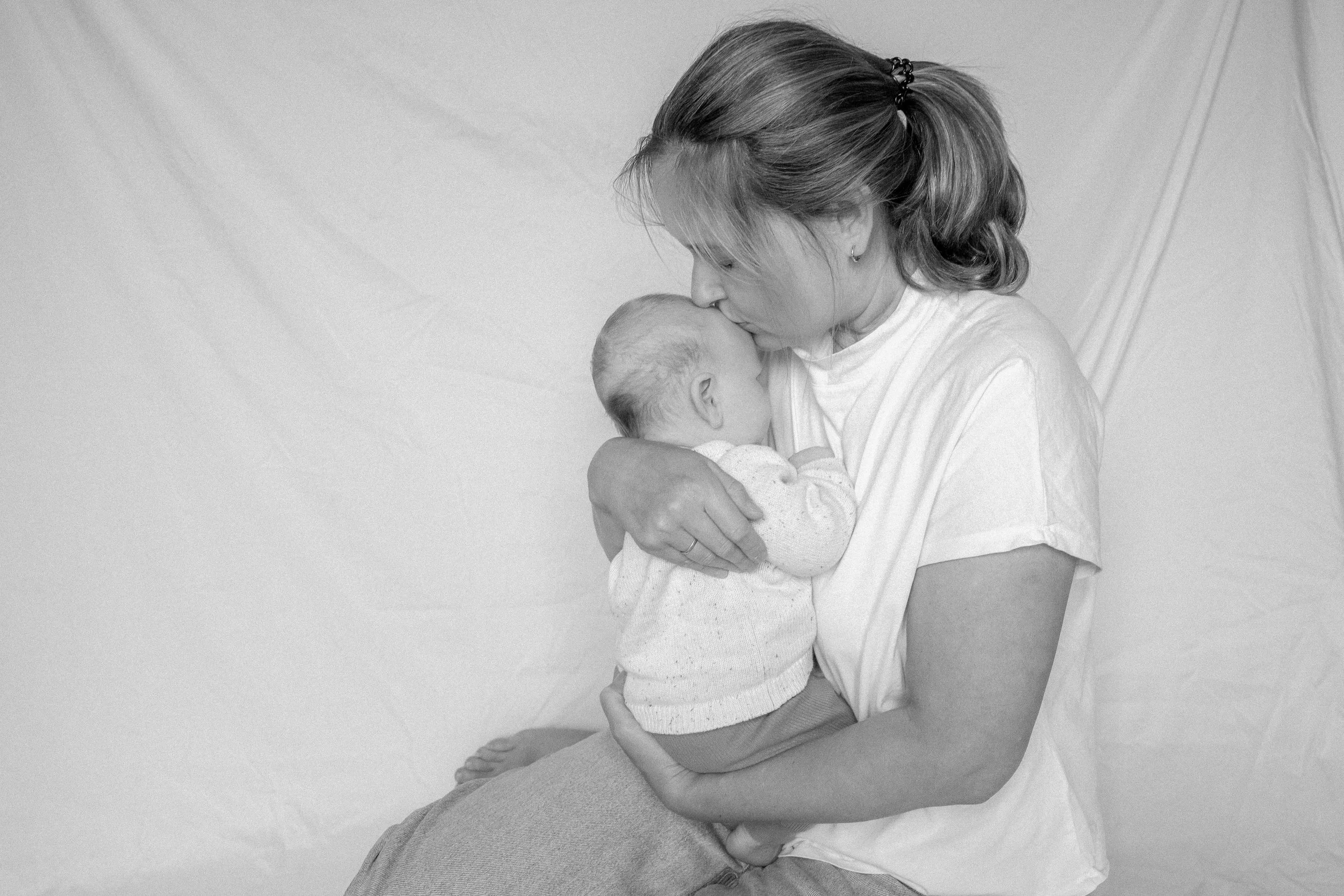 Eine Frau hält ein neugeborenes Baby in den Armen und küsst es liebevoll auf die Stirn, schwarze und weiße Aufnahme.