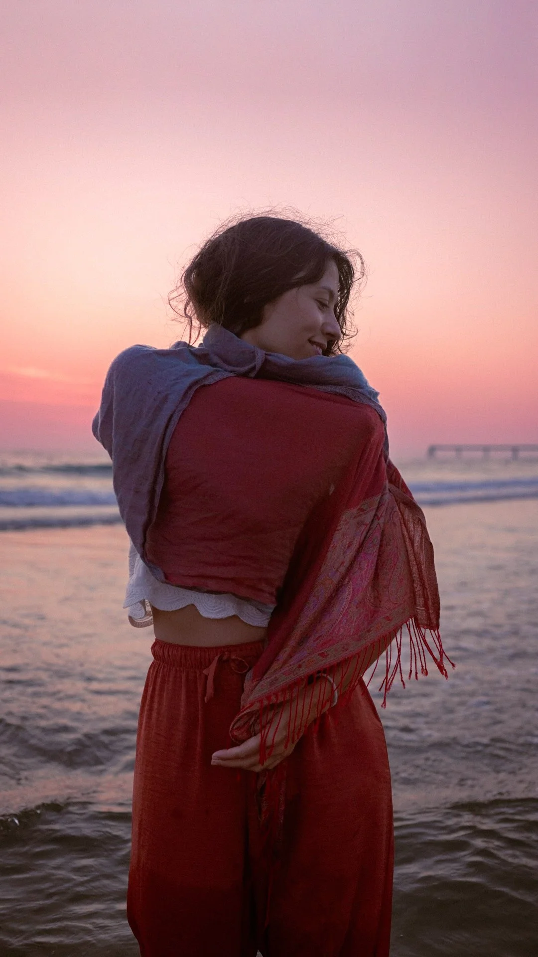 Éloïse enveloppée dans une écharpe, sur la plage au coucher du soleil