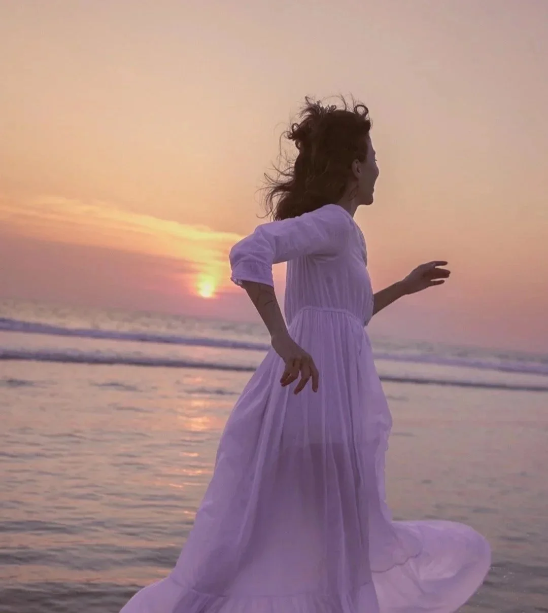 Femme en robe blanche courant sur la plage au coucher du soleil