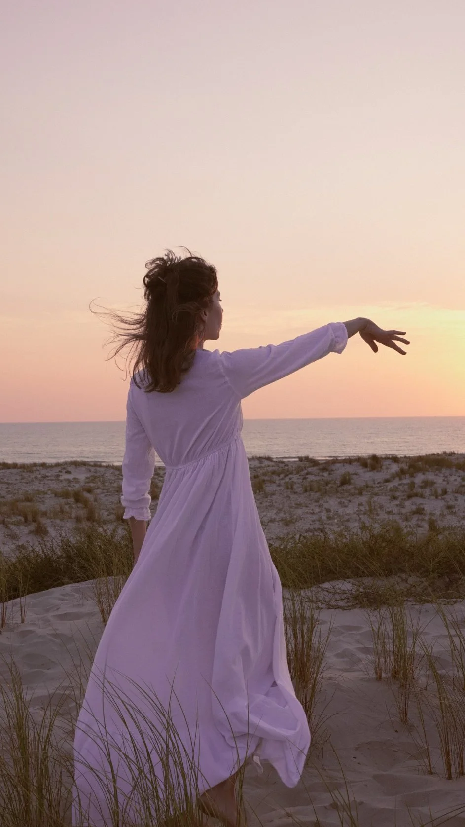 Éloïse en robe blanche dans les dunes, bras tendu vers l'horizon
