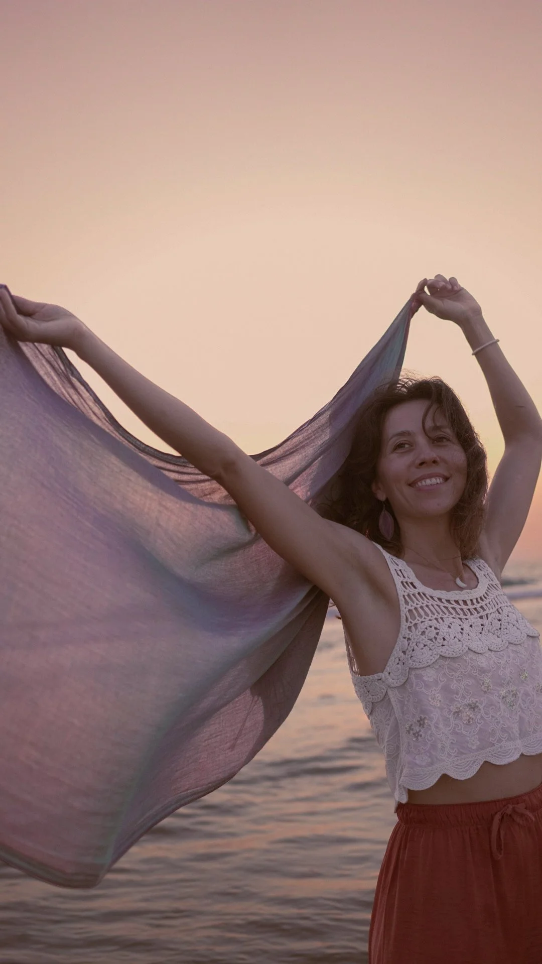 Éloïse tenant une écharpe qui vole au vent, sourire, plage au coucher du soleil