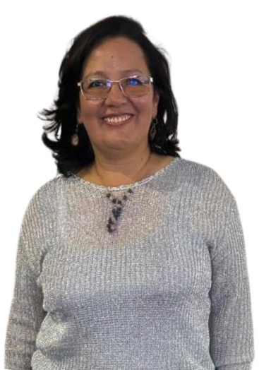 A smiling woman with shoulder-length dark hair, wearing glasses, a silver sweater, and earrings, standing against a white background.