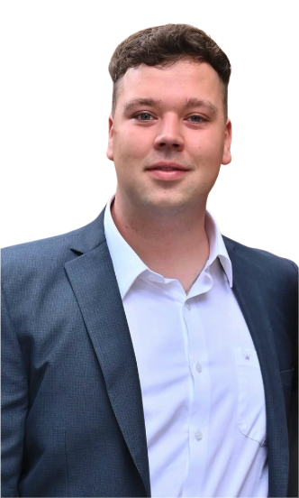 A young man with short dark hair, wearing a blue suit jacket and a white button-up shirt, standing against a plain white background.